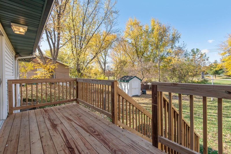 Wooden deck with a picket railing off the back of a house, looking over an autumn backyard