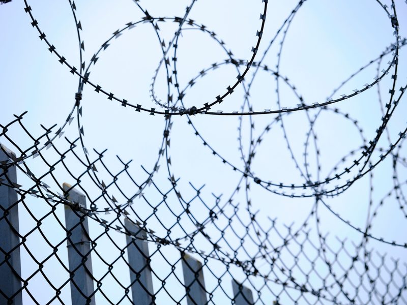 Chain-link security fence topped with coils of razor wire against a pale sky