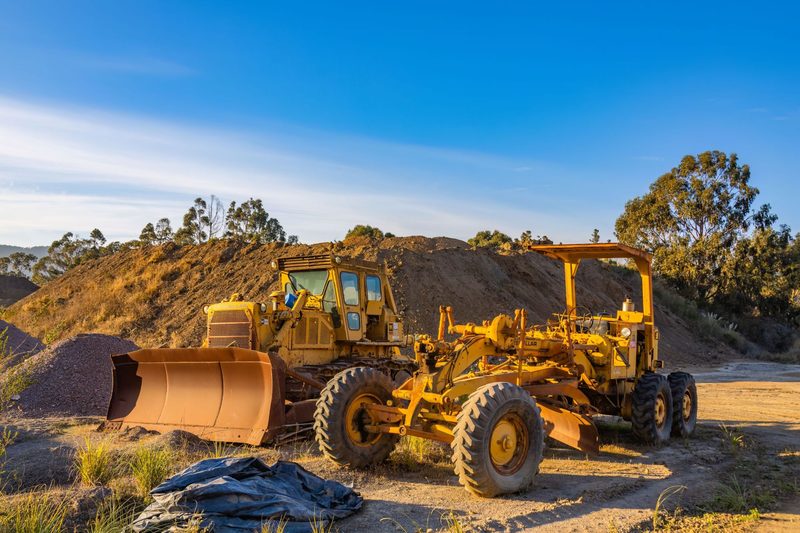 Bulldozer and motor grader parked on a cleared dirt site beside earth mounds