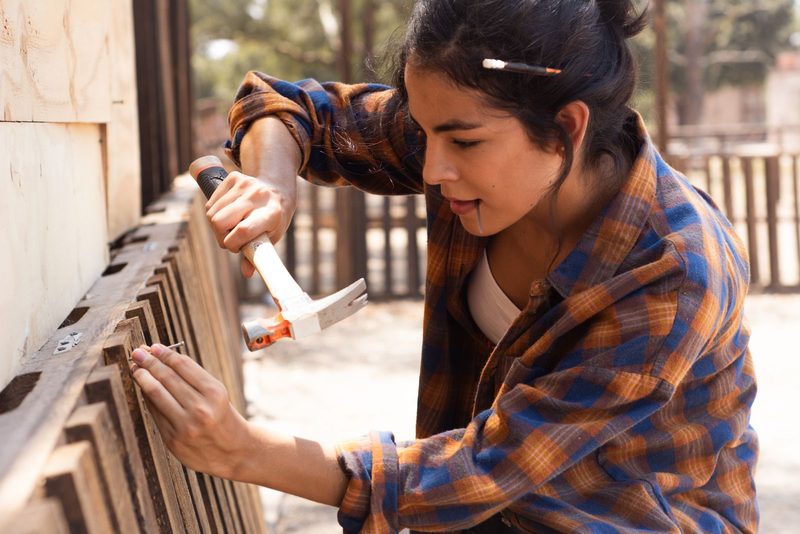 Carpenter hammering a nail into a wooden fence