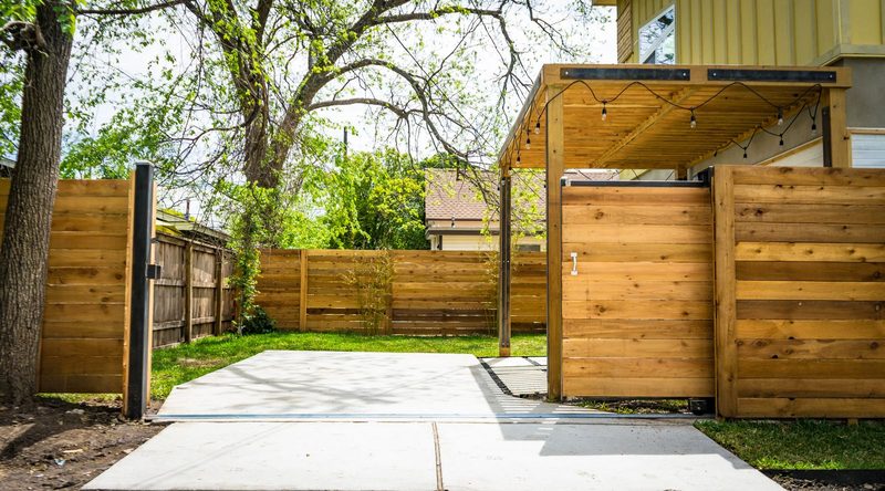 Horizontal cedar fence with a matching gate beside a concrete patio and a pergola in a sunny backyard