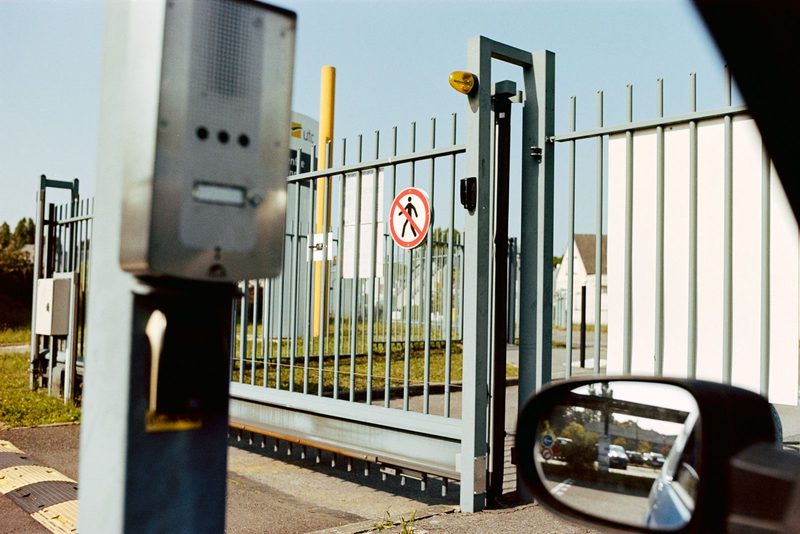 Sliding steel security gate and an intercom post, seen from a car window at the entrance