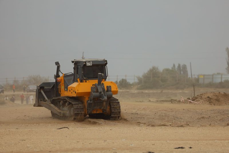 Yellow crawler bulldozer working a flat, dusty site with a fence line behind